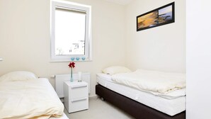 A hotel room with two beds, a window, a bedside table with a vase, and a framed picture on the wall. - Holiday Home in Grossenbrode (Grossenbrode)