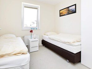 A hotel room with two beds, a window, a bedside table with a vase, and a framed picture on the wall. - Holiday Home in Grossenbrode (Grossenbrode)