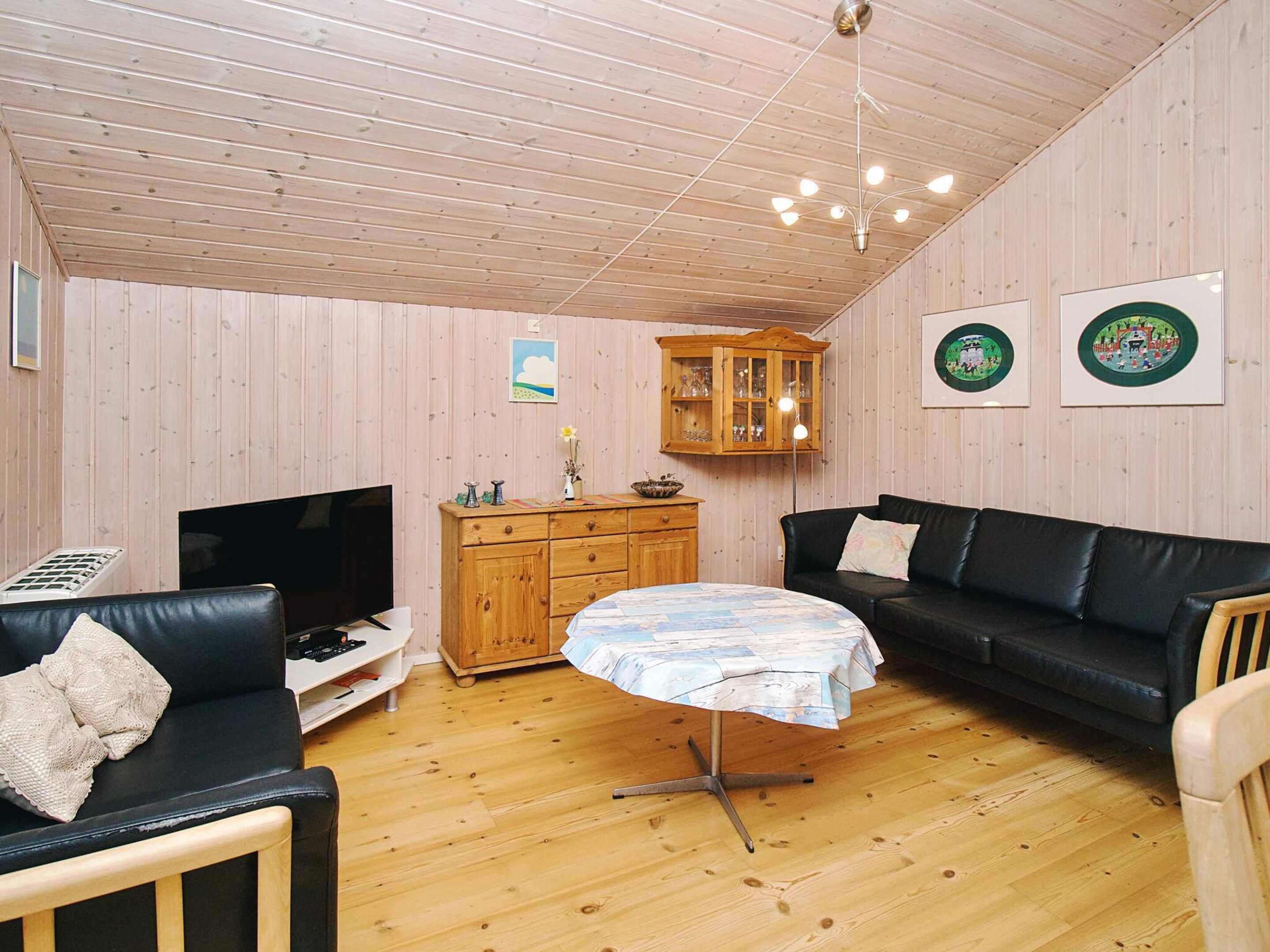 Un salon chaleureux avec un plafond en bois, un canapé en cuir noir, une petite table ronde et un meuble en bois.