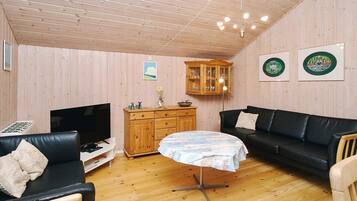 Un salon chaleureux avec un plafond en bois, un canapé en cuir noir, une petite table ronde et un meuble en bois.