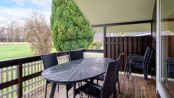 Un patio cubierto al aire libre con una mesa redonda y sillas, una terraza de madera y vistas del paisaje circundante.