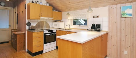 A compact kitchen with wooden cabinets, a stove, a microwave, and a coffee maker.
