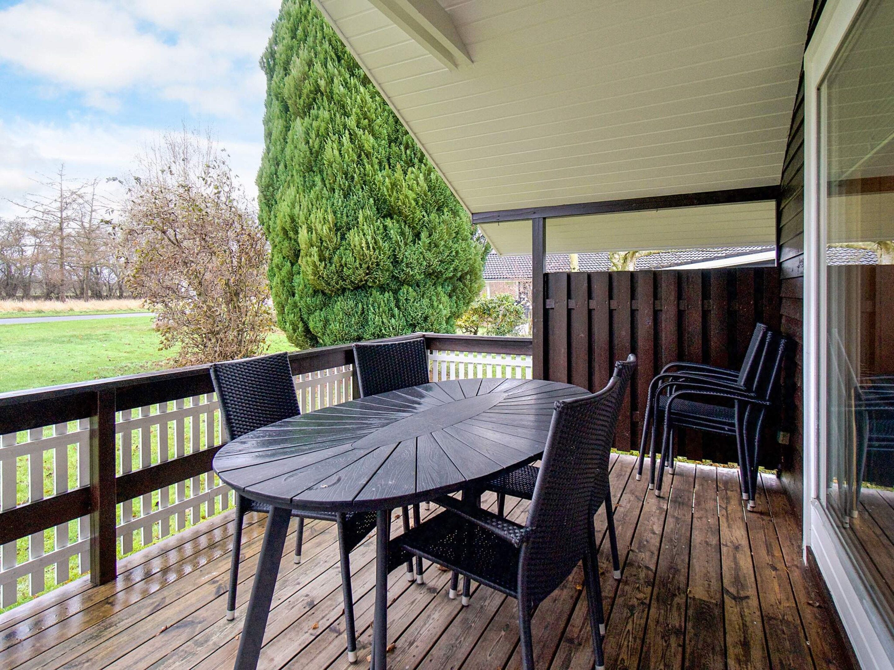 Un patio techado con una mesa redonda y sillas, una terraza de madera y vistas del entorno.