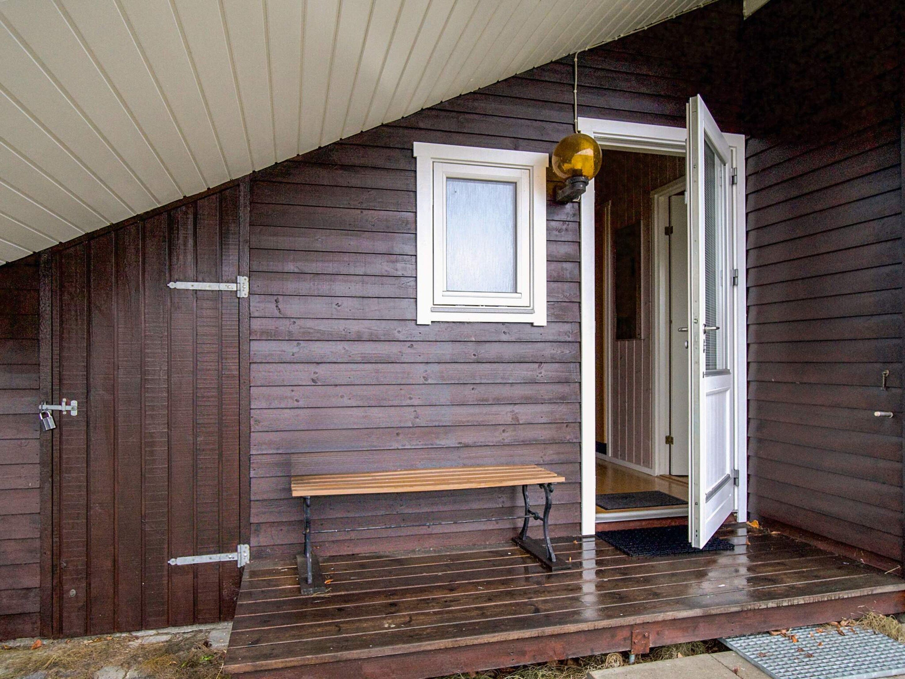 A wooden exterior with a bench, a door, and a hanging light fixture.