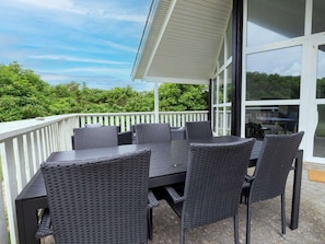 An outdoor patio with a table and chairs, a white railing, and a view of greenery. - 4 Star Holiday Home in Harboore (Harboore)