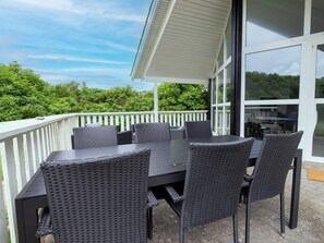 A covered outdoor patio with a table and chairs, a white railing, and a view of greenery. - 4 Star Holiday Home in Harboore (Harboore)