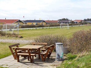 Ein Picknickplatz mit Bänken und einem Mülleimer, ein Fußballfeld mit Toren und Häuser im Hintergrund.