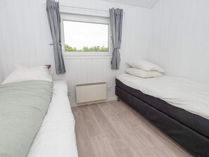 Ein Schlafzimmer mit zwei Betten, einem Fenster mit Vorhängen, einem Heizkörper und Blick ins Grüne.