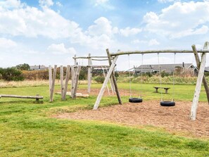 Ein Spielplatz mit Schaukeln und einer Fahrradschaukel, umgeben von Gras und einem Feldweg.