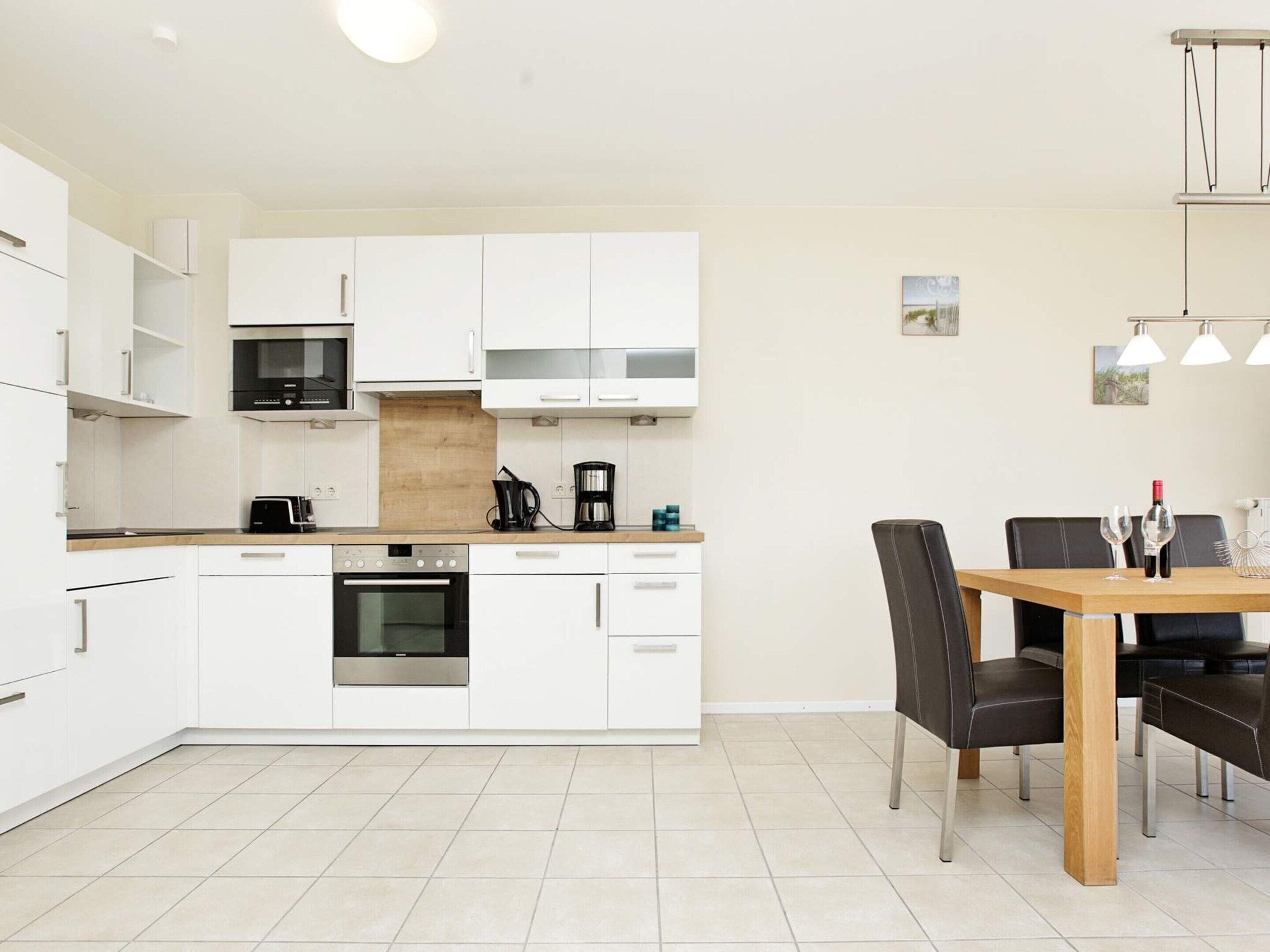 Une cuisine moderne avec des meubles blancs, un four encastré et un coin repas comprenant une table et des chaises en bois.