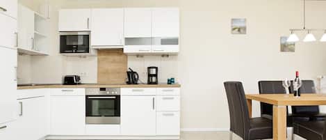 Una cocina moderna con armarios blancos, horno empotrado y comedor con mesa y sillas de madera.