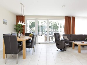 A modern living room with a dining area, featuring a sofa, chairs, a table, and a view through large glass doors. - Holiday Home in Großenbrode (Grossenbrode)