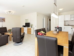 Una sala de estar moderna con un sofá, una mesa de comedor con sillas, un televisor y una cocina con armarios y una encimera.