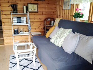 A cozy room with a sofa, a small white table, a shelf with various items, and a window with a view.