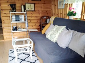A cozy room with a sofa, a small white table, a shelf with various items, and a window with a view. - 4 Person Holiday Home in Ekero (Ekerö)