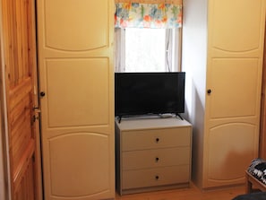 A room with a television on a cabinet, wooden doors, and a window with a floral curtain. - 4 Person Holiday Home in Ekero (Ekerö)