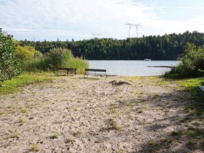 Una playa arenosa con dos bancos, un lago y un área boscosa al fondo.