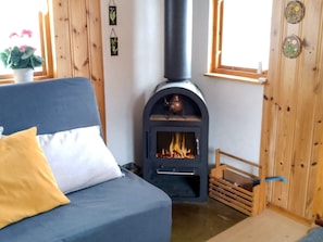 A room with a blue sofa, a wooden wall, a black wood stove, and a window. - 4 Person Holiday Home in Ekero (Ekerö)