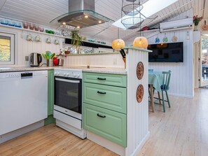 A modern kitchen with white and green cabinetry, a built-in oven, and a dining area with a table and chairs. - 4 Star Holiday Home in Ansager (Ansager)