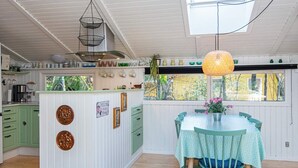 A kitchen with a central island, a dining area with a table and chairs, and a view of the outside through large windows. - 4 Star Holiday Home in Ansager (Ansager)