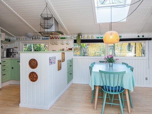 Una cocina con una isla central, un comedor con mesa y sillas, y vistas al exterior gracias a amplios ventanales.