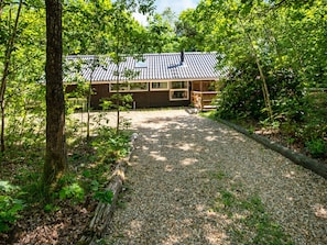 A wooden cabin with a gravel driveway, surrounded by dense forest. - 4 Star Holiday Home in Ansager (Ansager)