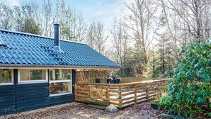 A cabin with a sloped roof, a wooden deck, and a gravel driveway. - 4 Star Holiday Home in Ansager (Ansager)