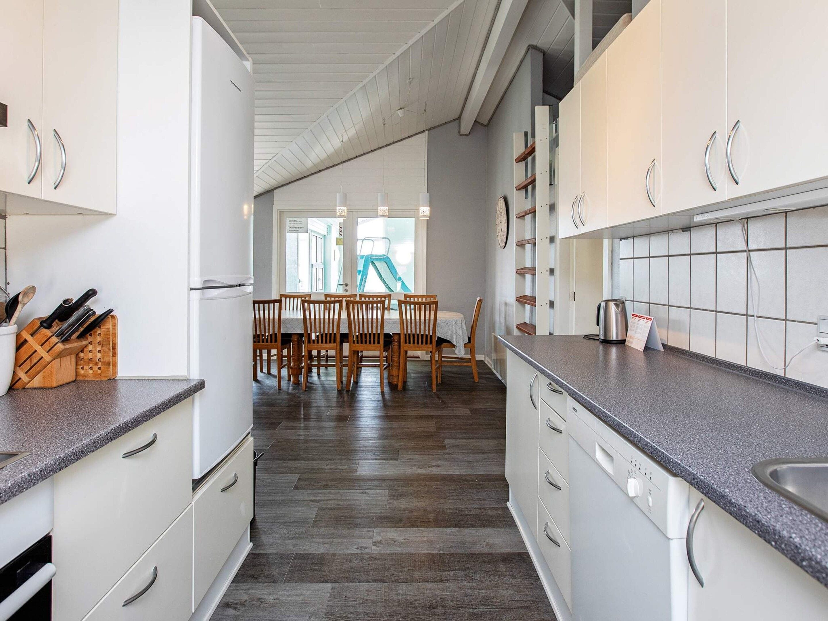 Een moderne keuken met witte kasten, een granieten aanrechtblad en een eethoek met houten stoelen en een tafel.