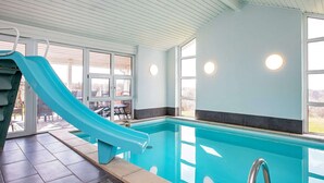 An indoor swimming pool with a blue slide, clear glass walls, and a tiled floor. - Spacious Holiday Home in Vestervig near Sea (Vestervig)