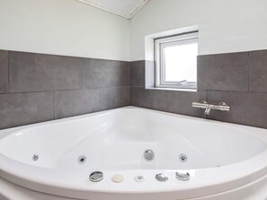 A modern bathroom with a large bathtub, a window, and grey tiled walls.