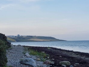 A coastal landscape with a rocky shoreline, a body of water, and a distant building on a hill. - Spacious Holiday Home in Vestervig near Sea (Vestervig)