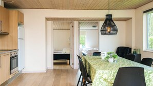 Ett modernt kök med träskåp, en matplats med bord och stolar och ett sovrum som syns genom en öppen dörr.