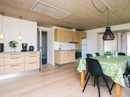 A modern kitchen with wooden cabinets, a dining area with a table and chairs, and a ceiling with exposed beams.