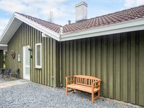 A building with a sloped roof, a wooden bench, and a gravel driveway.