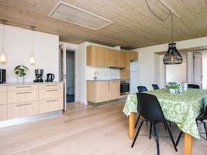 A modern kitchen with wooden cabinets, a dining table with chairs, and a hanging light fixture. - 4 Person Holiday Home in Borkop (Borkop)