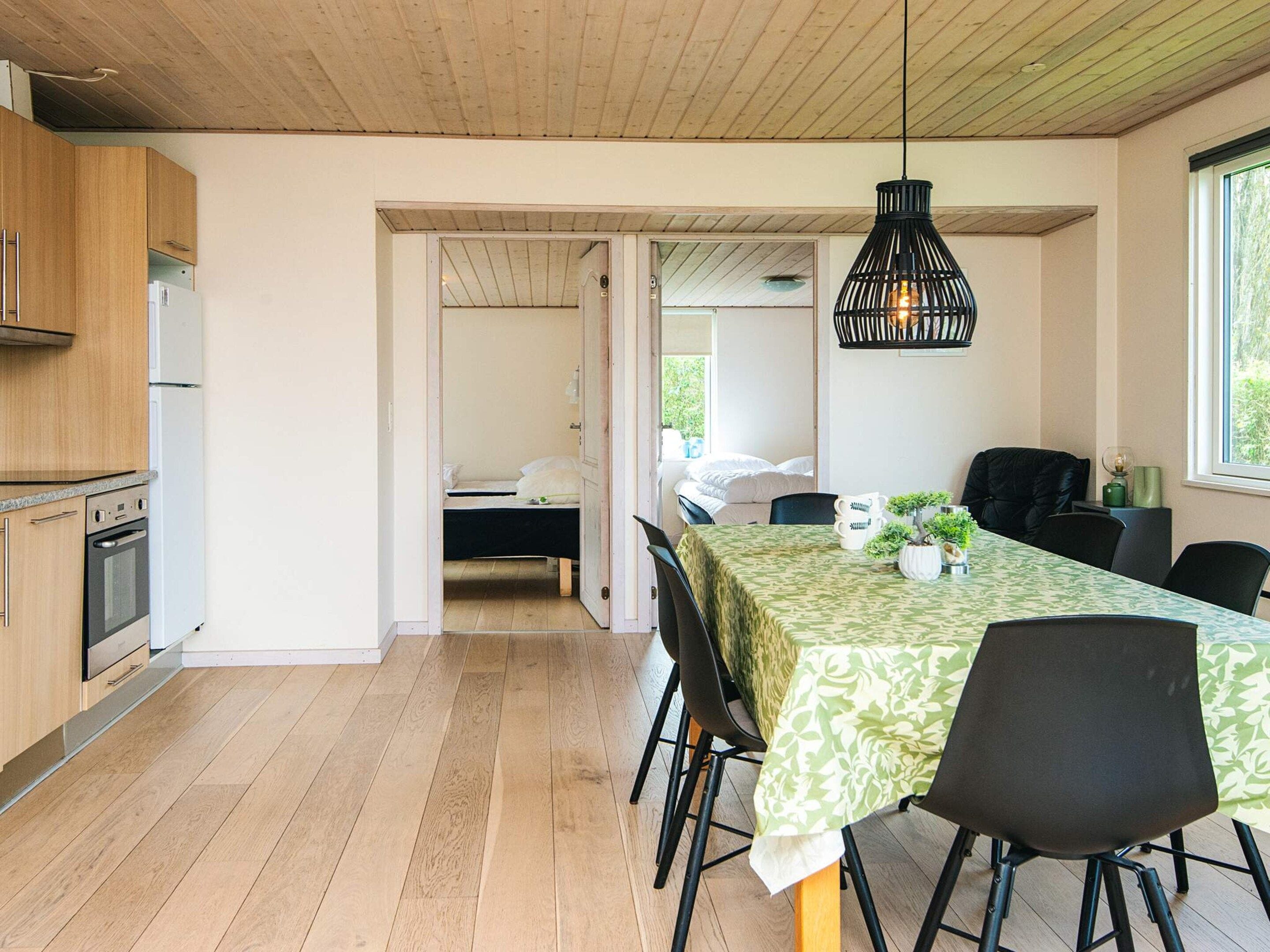 A modern kitchen with wooden cabinets, a dining table with chairs, and a hanging light fixture.