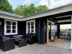 A covered outdoor area with a dining table and chairs, a wicker sofa, and a window with a view of the landscape.