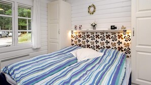 A bedroom with a bed, a window with curtains, a wall with a floral pattern, and a shelf with decorative items.