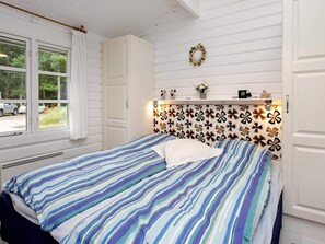 A bedroom with a bed, a window with curtains, a wall with a floral pattern, and a shelf with decorative items.