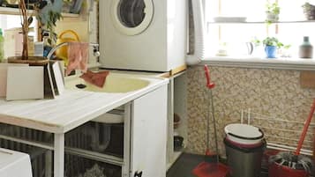 Un espace buanderie comprenant un lave-linge, un évier, un balai et une poubelle.