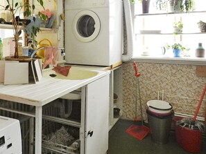 A laundry area with a washing machine, a sink, a broom, and a trash can.