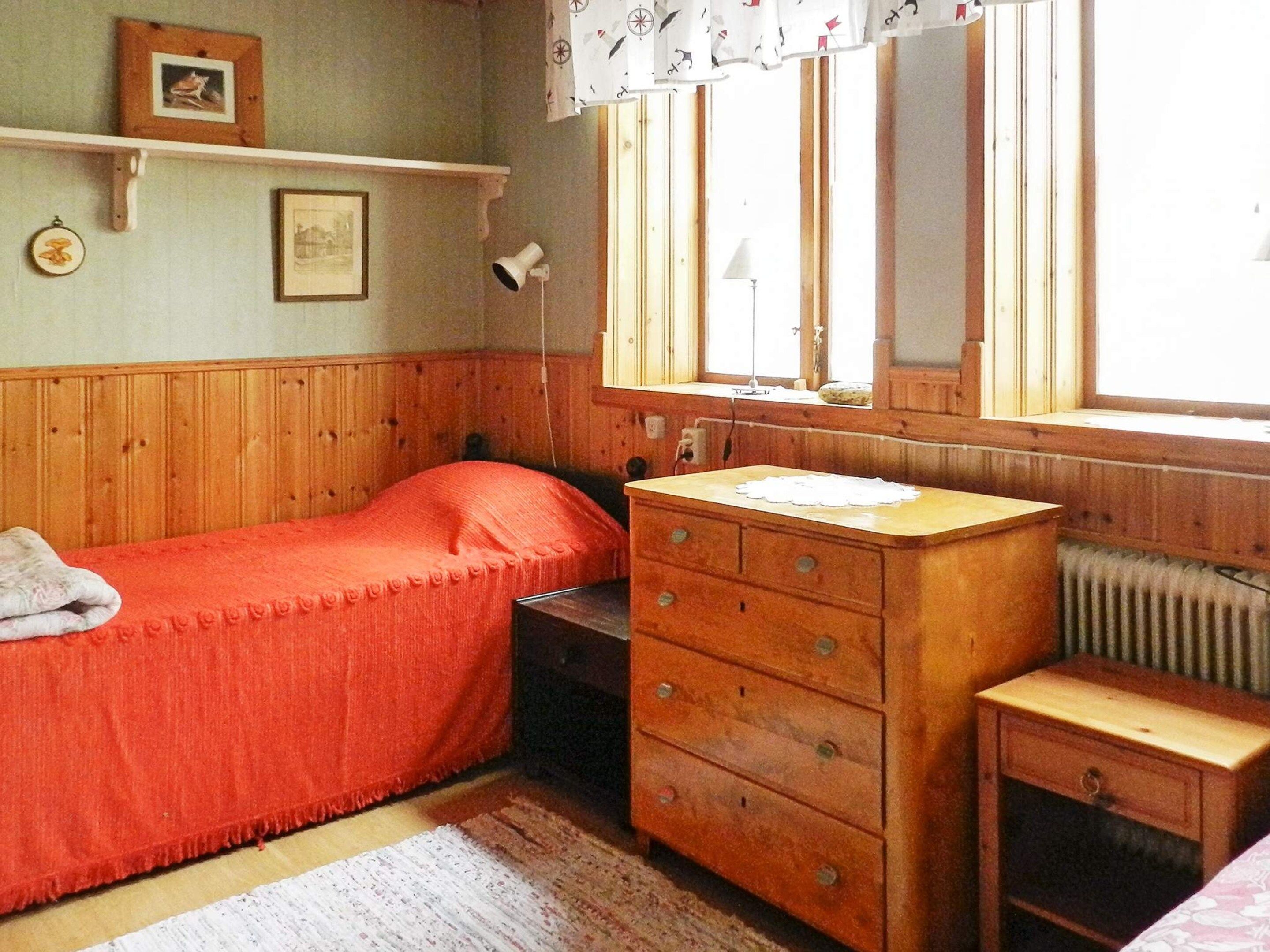 A small, cozy bedroom with a single bed, a wooden dresser, and a window with curtains.
