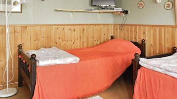 A room with a wooden-paneled wall, a bed with an orange bedspread, a television on a shelf, and a white floor lamp.
