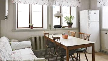 A cozy living room with a sofa, a dining table with chairs, a radiator, and a white refrigerator.