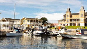 A marina with boats docked, a building with a balcony, and a grassy area in the background. - 3 Person Holiday Home in Lysekil (Lysekil)