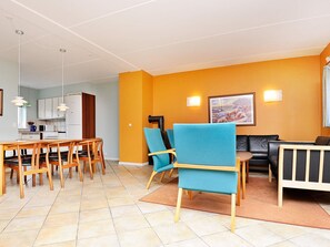 Un salon moderne avec un coin repas, comprenant un canapé, des fauteuils et une cuisine en arrière-plan.