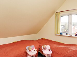 Una habitación con dos camas, una ventana con cortinas y dos muñecas en sillas altas.
