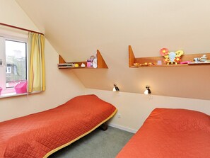 Une chambre avec deux lits simples, une fenêtre avec des rideaux jaunes et des étagères remplies de divers objets.