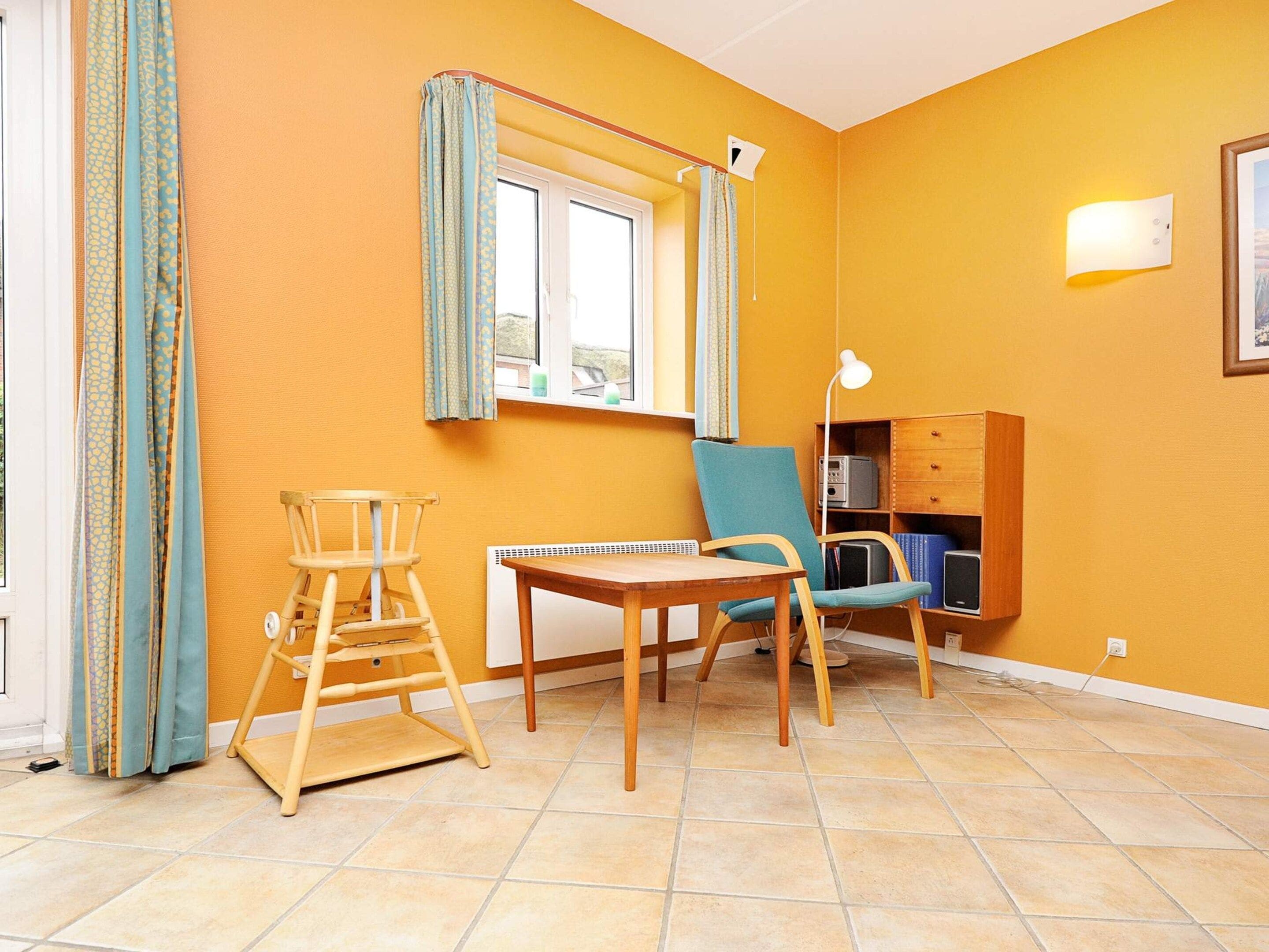 A room with a window, a table, two chairs, a lamp, and a bookshelf.