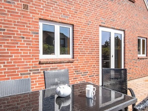 A glass table with a white teapot and two white cups, set against a brick wall with two windows and a door. - 4 Star Holiday Home in Blavand (Blavand)